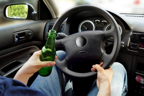 underage drinking and driving - teenager behind the steering wheel holding a bottle of beer
