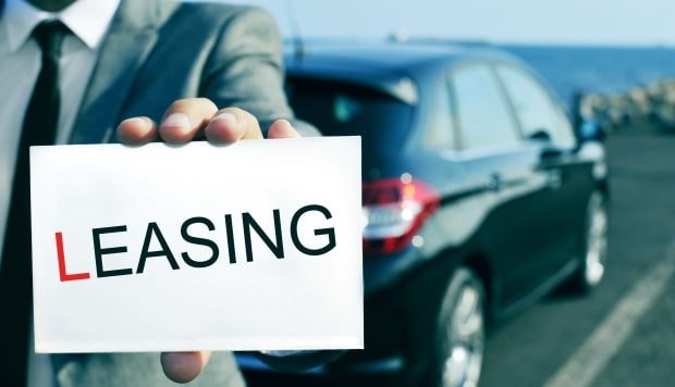 leasing a car - man holding a leasing sign in front of new car