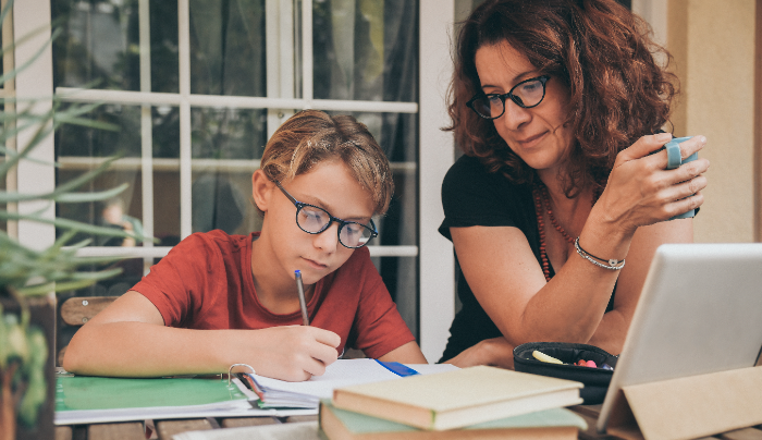 Homeschooling decision for families-Young student doing homework at home with school books newspaper, digital pad helped by his mother.