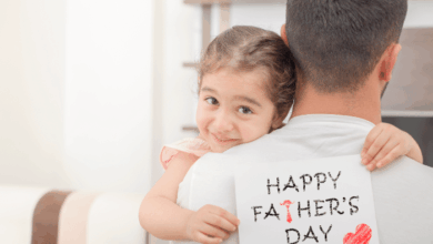 Honoring Fathers And Stepfathers-little girl hugs his father and shows happy fathers day card