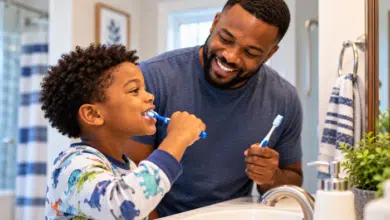 A bathroom scene showing a stepdad and his elementary-school-age stepchild brushing his teeth in front of the mirror